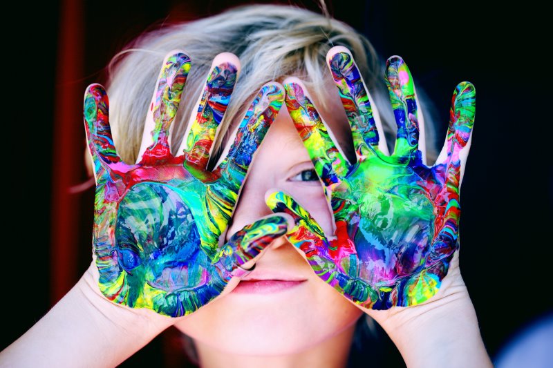 Kind mit farbigen Händen vor dem Gesicht