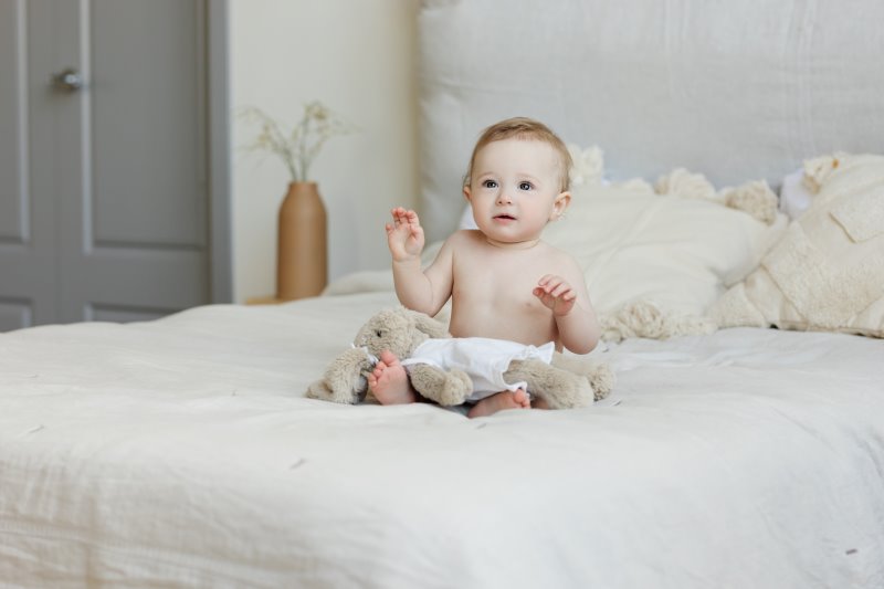 Ein Baby sitzt auf einem weißen Bett mit einem Stofftier