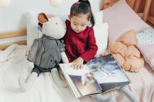 Kind liest Kinderbuch mit Kuscheltier