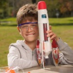 Kind mit Sicherheitsbrille und Rakete aus dem Experimentierkasten