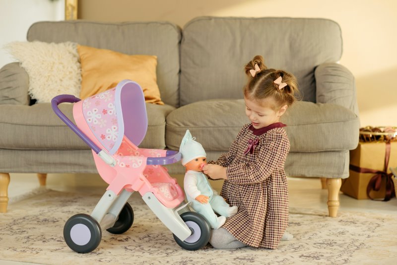 Mädchen spielt mit einer Puppe und einem Puppenwagen
