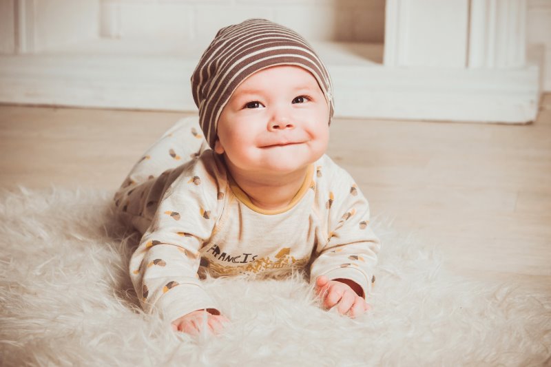 Ein lächelndes Baby mit einem beigen Strampelanzug und einer braun weiß gestreiften Mütze