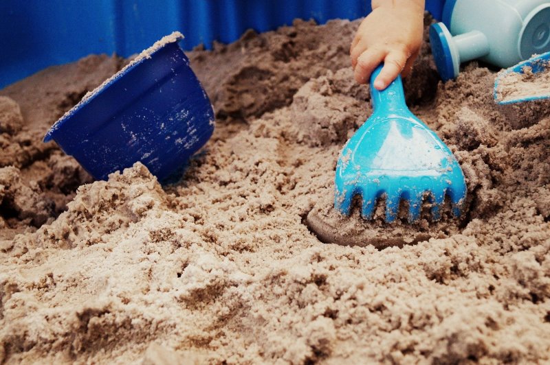 Kinderhand spielt im Sand mit einer Hake
