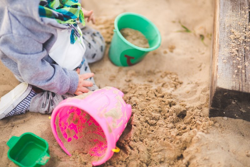 Kleinkind spielt mit bunten Eimern im Sandkasten